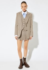 Tämä on ruudullinen puku beige sävyissä, joka koostuu kaksirivisestä bleiseristä ja vastaavasta hameesta. Sopii ruskeiden nilkkureiden ja vaaleansinisen paidan kanssa.