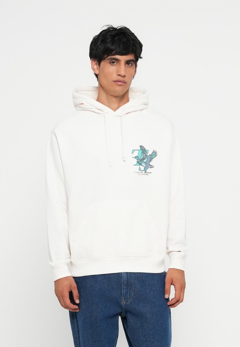 Weißer Hoodie mit einer Fronttasche, ausgestattet mit einem türkisfarbenen Grafiklogo auf der Brust. Der Stoff sieht weich aus und hat eine Kapuze mit Kordelzug. Kombiniert mit blauen Jeans.