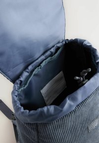 Blå corduroy taske med snørreåbning, blød foer og et indre label til kontaktinformation. Glat overflade og struktureret form.