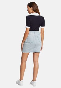 Polo shirt noir à manches courtes avec col blanc, associé à une jupe en denim bleu clair, arborant une silhouette ajustée et des poches arrière.