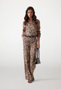 Blouse à imprimé léopard et pantalon large assorti, tous deux en tissu lisse, complétés par une ceinture noire et un petit sac à main.