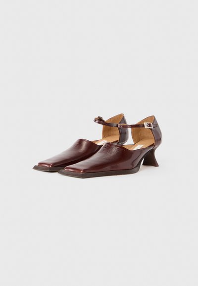 Scarpe in pelle bordeaux con punta affusolata, cinturino alla caviglia e un lieve tacco curvato. Texture liscia e design minimalista.