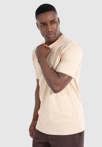 Beige kortærmet T-shirt med rund halsudskæring, lavet af blødt bomuldsmateriale, har en afslappet pasform og minimale sømme for et glat udseende.