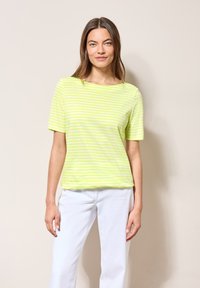 Tričko s krátkým rukávem v barvě limetkové zelené s pruhy, uvolněný střih, kulatý výstřih a měkká textilie, ve spojení s bílými kalhotami.