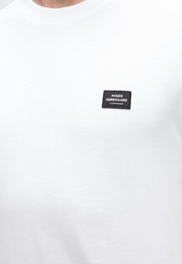 Λευκό T-shirt με ένα μικρό μαύρο ορθογώνιο λογότυπο στο στήθος με την ένδειξη «MADS NØRGAARD COPENHAGEN.»