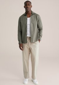 Hemd in olijfgroen katoen, met knoopsluiting en een ontspannen pasvorm. Gecombineerd met beige rechte broek en witte sneakers. Soepele textuur.