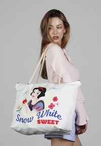 Sac en toile représentant un design de Blanche-Neige, avec des poignées en corde, des accents floraux colorés, et le texte "Blanche-Neige DOUCE." Fond blanc.