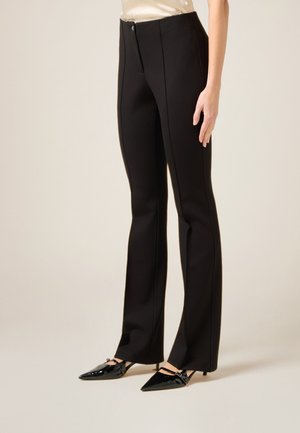 Sorte skræddersyede bukser med en strømlinet pasform, der har et glat stof, lynlås foran og lodrette sømdetaljer. Kombineret med spidse sorte hæle.