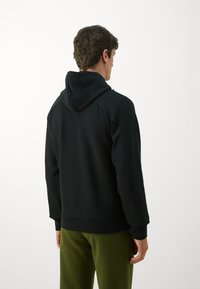 Schwarzer Hoodie mit lässiger Passform, ausgestattet mit einer Kordelzugkapuze und gerippten Bündchen, kombiniert mit olivgrünen Hosen, von hinten gezeigt.