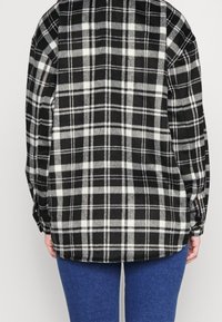 Black and white plaid flannel shirt with a relaxed fit, long sleeves, and buttoned cuffs. Soft texture and visible stitching details.