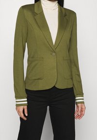 Blazer verde oliva realizzato in materiale morbido, con un taglio sartoriale, due tasche frontali e rifiniture a righe sui polsini.