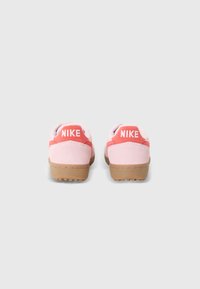 Rosa semskede sko med gummisåle, med en kontrasterende rød detalj og "NIKE" logo på hælen. Glatt tekstur.