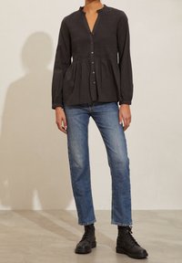 Svart långärmad blus med smockad kropp, volangkrage och knäppning fram. Kombinerad med blå raka jeans och svarta snörstövlar.