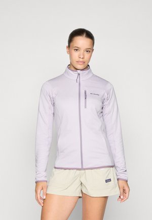 Lys lilla zip-up jakke med høy krage, strukturert stoff og brystlomme. Kombinert med beige shorts med sidelommer.
