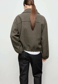 Chaqueta marrón de pata de gallo recortada con cuello de solapa, dobladillo elástico y hombros caídos, combinada con jeans oscuros.