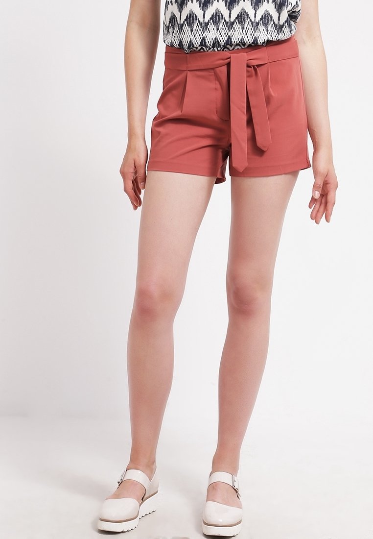Pantaloni corti color ruggine con vita alta, dettaglio con cintura annodata e due tasche laterali. Il materiale appare liscio con un taglio su misura.
