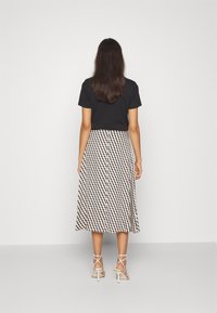 T-shirt noir court associé à une longue jupe à motifs avec un design en losanges beige et marine, complété par des talons blancs à lanières.