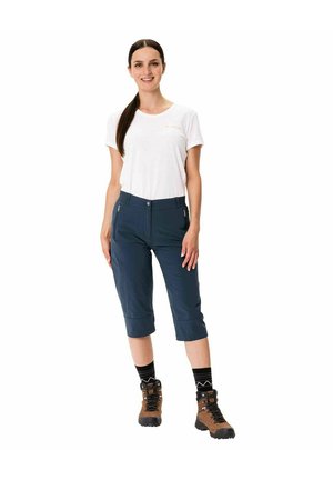 Marineblau Caprihosen mit vier Taschen, aus leichtem Material. Kombiniert mit einem weißen T-Shirt und braunen Wanderschuhen sowie schwarzen Socken.