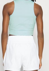 A mint green cropped tank top features a smooth texture, paired with white shorts that have a gathered elastic waistband.