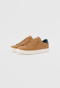 Brown leather sneakers with a smooth texture, round toe, and white rubber sole. Features round laces and a navy accent on the heel.