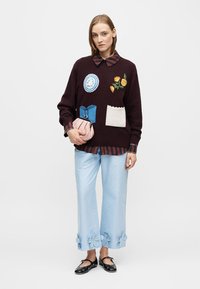 Burgunderfarget strikket genser med broderte lapper; blåstripet skjorte under. Lyseblå satengvide bukser med blomsterdetaljer. Sorte sko.