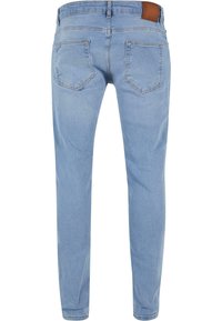 Jean en denim bleu clair coupe slim, avec deux poches arrière, une étiquette en cuir marron à la taille, et une texture lisse.