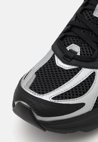 Black athletic shoe featuring a mesh upper with silver accents, a padded collar, and a textured rubber sole. Rounded toe design with supportive overlays.
