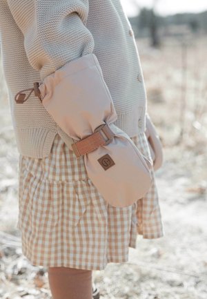 Beige mittens with a textured fabric, secured by a brown strap featuring a logo, paired with a light sweater and checked dress.
