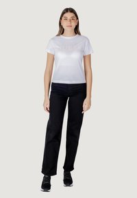 Witte t-shirt met korte mouwen met het "GUESS" logo, gecombineerd met zwarte rechttoe-rechtaan jeans en zwarte sportschoenen. Eenvoudig, modern ontwerp.