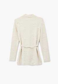 Cremefarvet, tekstureret langærmet jakke med krave og et tyndt bælte bundet i taljen, vist fra bagsiden på en hvid baggrund.