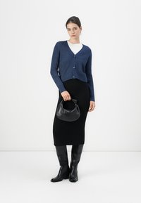 Navy knitted cardigan with a v-neck, button closure; black fitted midi skirt; black knee-high boots; black handbag with a rounded shape.