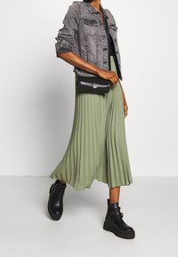 Denimjacka i grått, plisserad midkjol i dämpat grönt, svarta ankelskor med spännen, och en liten svart crossbody-väska.