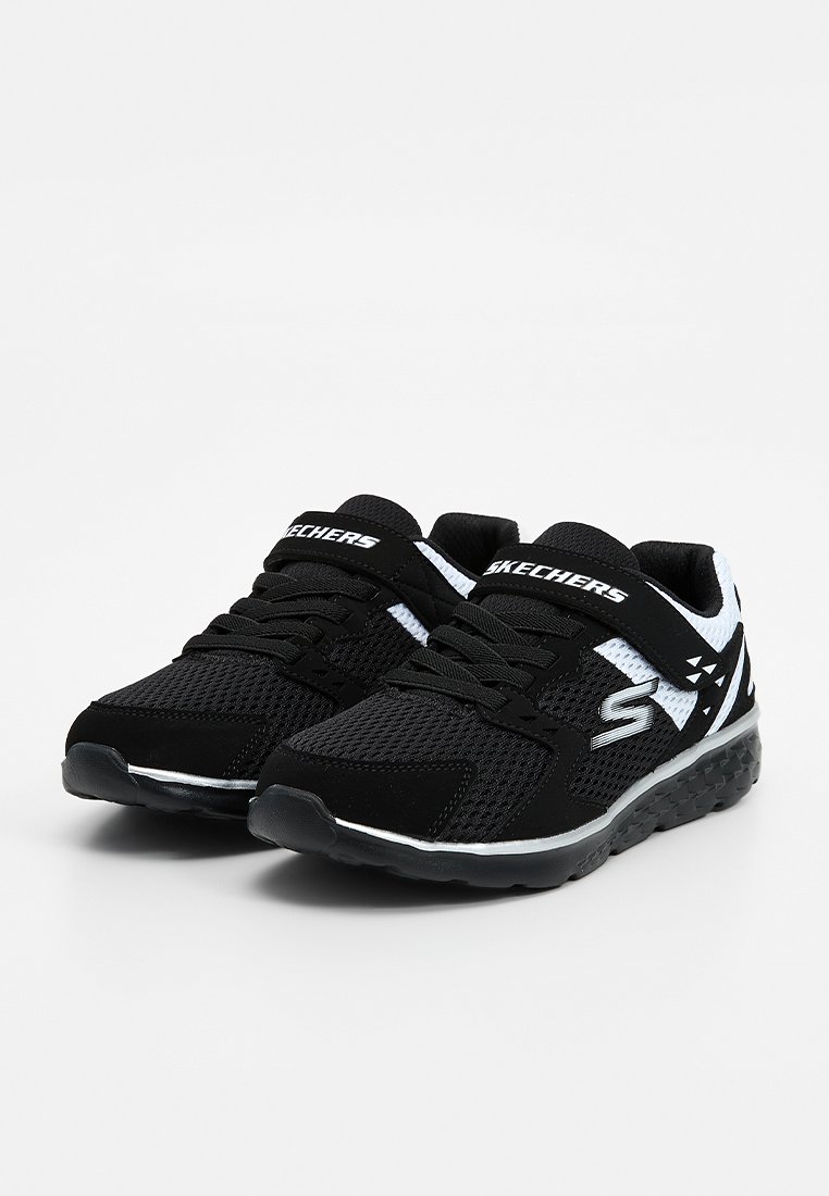 Zapatillas deportivas Skechers en blanco y negro con tejido de malla, cordones y cierres de velcro sobre un fondo blanco.