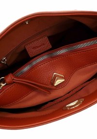 Interior de un bolso de mano de cuero texturizado en rojo, con un bolsillo con cremallera y una etiqueta con el logo, forrado de manera suave y con acentos de hardware en tono dorado.