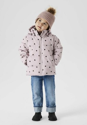 Giubbotto imbottito rosa chiaro con motivi a cuore neri, chiusura con zip, abbinato a jeans in denim blu e stivali neri alla caviglia. Cappello di maglia con pom-pom.