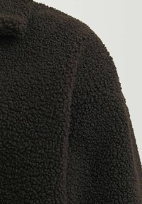 Schwarzer Fleece-Mantel aus strukturiertem, kuscheligem Material mit Kragen, der ein weiches, warmes Aussehen unterstreicht. Keine sichtbaren Beschläge oder Muster.