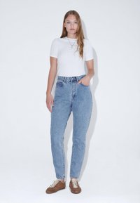 Světle modré džíny s vysokým pasem a rovnými nohavicemi, s knoflíkovou légou a jemným opotřebením. Doplněné o přiléhavé bílé tričko.