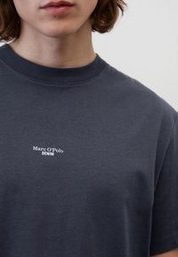 Sötétszürke pamut póló kerek nyakkal, melyen fehér "Marc O'Polo DENIM" logó található a mellrészen. Rövid ujjú.