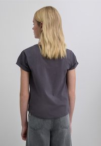 Camiseta de manga corta en algodón suave de color gris oscuro con un corte holgado. El dobladillo se curva ligeramente en la parte trasera; cuenta con mangas arremangadas.