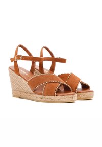 Bruine suede wijdte sandalen met kruisbanden, gouden kraalaccenten en een geweven jute zool. De hakhoogte is gemiddeld, wat zorgt voor een stabiele basis.