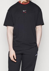 Person wearing a black Nike Air t-shirt and black Nike sweatpants with hands relaxed, standing against a plain background.