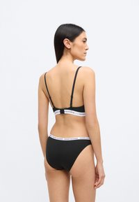 Fekete bralette állítható pántokkal és fehér TOMMY HILFIGER logós alsópánttal, hozzá illő fekete bikini alsóval, minimalista kialakítással.