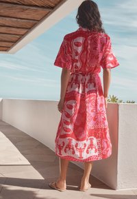 Robe midi à motifs rouges et roses, manches courtes, taille cintrée, avec des motifs floraux et marins. Le tissu semble léger et aérien.