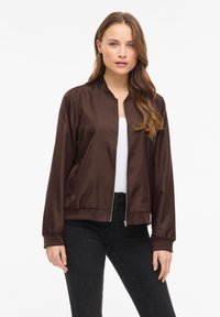 Brązowa kurtka typu bomber z satyny z kołnierzem typu stójka, zamkiem błyskawicznym z przodu i bocznymi kieszeniami. Posiada elastyczne mankiety i ściągacz na dole dla dopasowanego kroju.