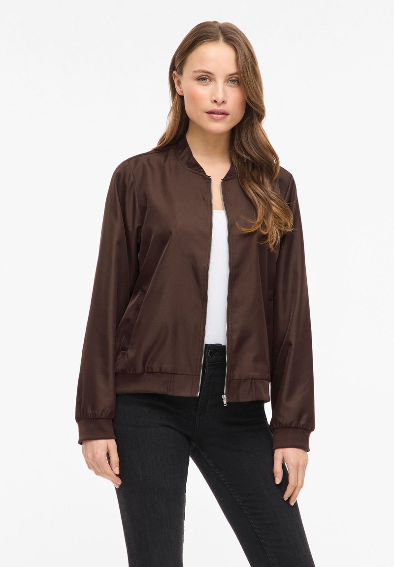 Brązowa kurtka typu bomber z satyny z kołnierzem typu stójka, zamkiem błyskawicznym z przodu i bocznymi kieszeniami. Posiada elastyczne mankiety i ściągacz na dole dla dopasowanego kroju.