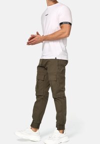 Hvid bomulds T-shirt med sort logo på ærmet, parret med olivengrønne cargo bukser med flere lommer og elastiske manchetter, båret med hvide sneakers.