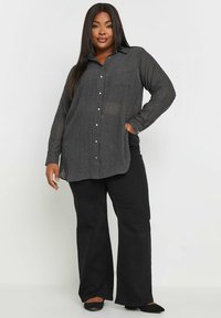 Zwarte doorschijnende button-up shirt met verticale strepen, lange mouwen en een losse pasvorm, gecombineerd met zwarte flared broeken en puntige flats.