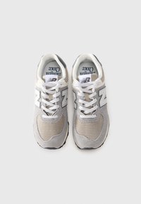 Une paire de baskets New Balance grises et beiges avec des lacets blancs, une texture en maille, et des logos "NB" sur les languettes et sur les côtés.