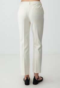 White tailored trousers with a slim fit, featuring back pockets and a smooth, lightweight fabric. Paired with black flats.