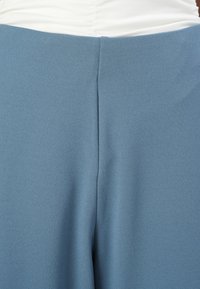 Lichtblauw stof, gladde textuur, op maat gemaakt ontwerp met een middennaad. Top in wit met gatherdetails zichtbaar boven de blauwe stof.